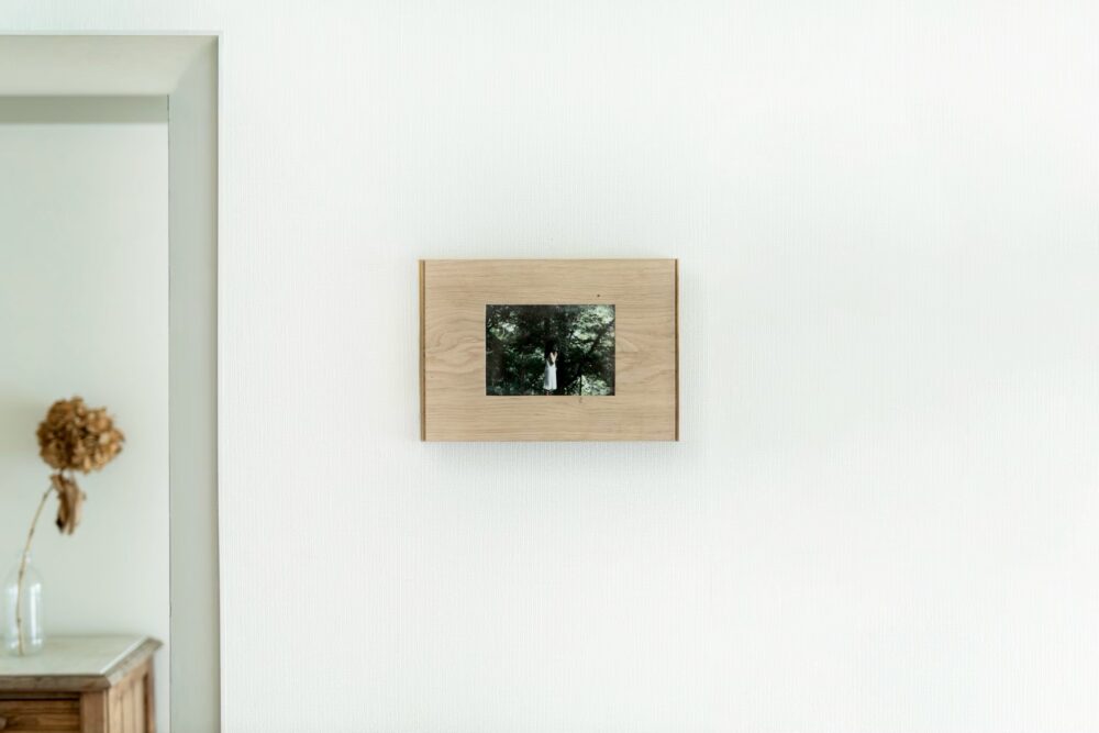 白い壁に掛けられた額縁　木の写真が収まっている